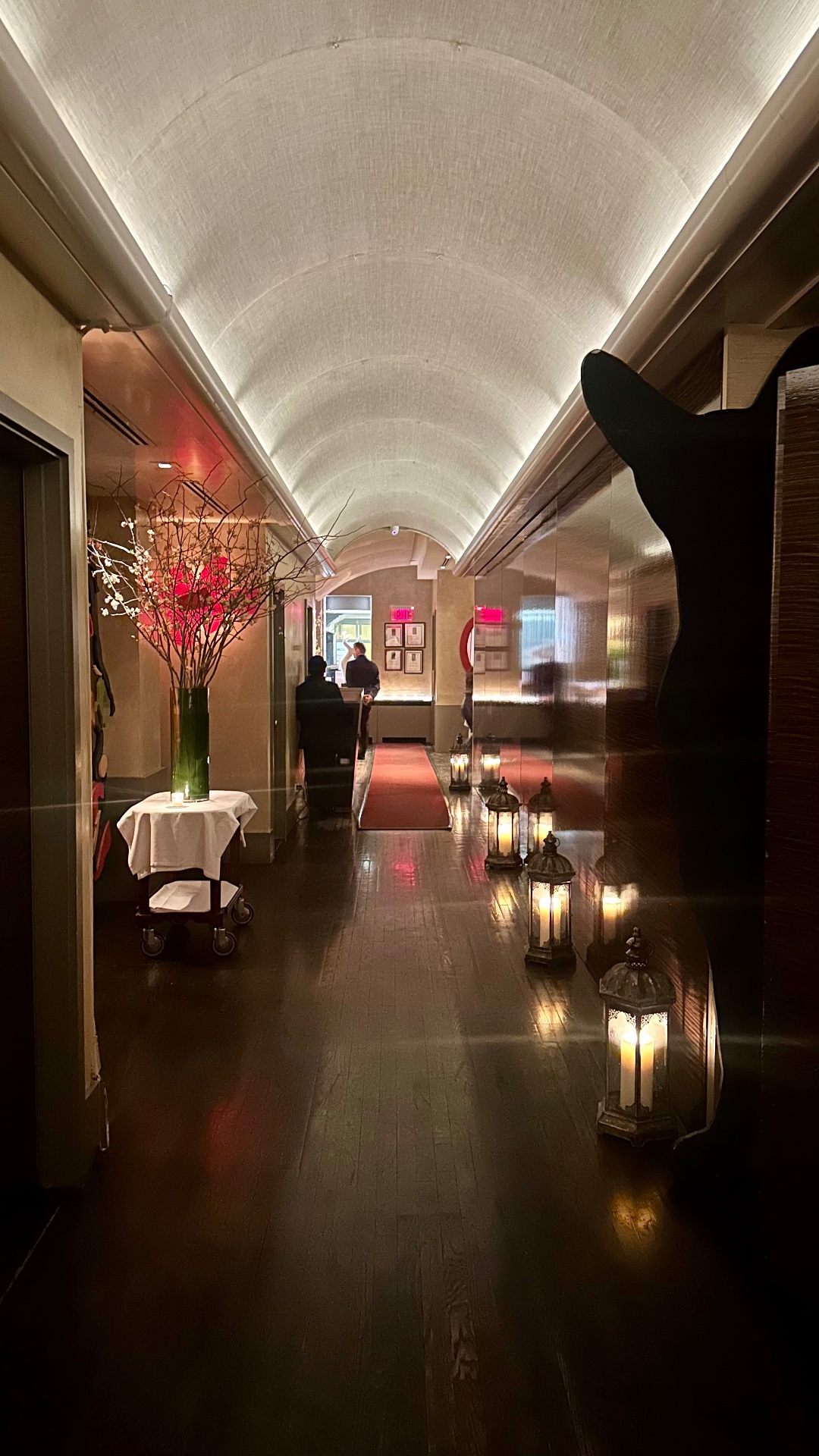 Farewell brunch entrance at Caravaggio — barrel-vaulted hallway lined with lanterns and pink branch florals